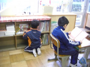 本棚の前で本を選ぶ男の子　傍らでは，静かに読書を進める姿が・・・。(8:05)