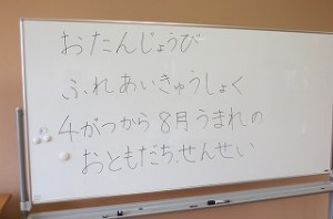 IMG_1666 ホワイトボードに「お誕生日 ふれあい給食 4~8月の生まれのお友達と先生」と書かれています。\